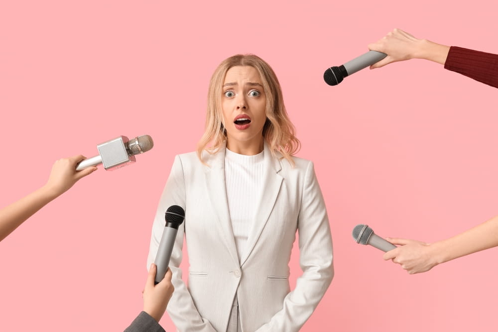 Woman under stress surrounded by microphones held out by unseen interviewers